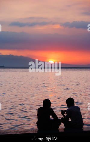 Silhouette di un giovane seduto sulla parete al tramonto sulla baia di Manila; Manila Filippine; Foto Stock