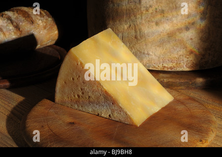 Cuneo di maturare il formaggio cheddar con a bordo tutto il formaggio e pane in background Foto Stock