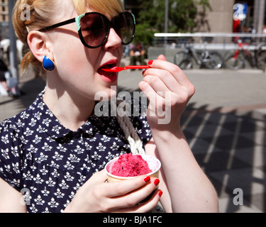 Ragazza bionda in funky sunnglasses rosa di mangiare il gelato in strada Foto Stock