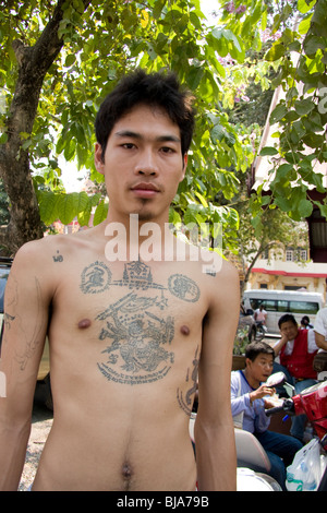 Un giovane uomo si mette in mostra il suo sacro di tatuaggi al Wat Phra Bang tempio in Thailandia, dove i monaci tattoo i loro devoti con preghiere. Foto Stock