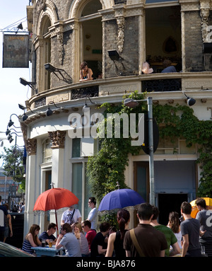 Le persone si sono riunite al di fuori di una casa pubblica e la donna appoggiata fuori da una finestra Foto Stock