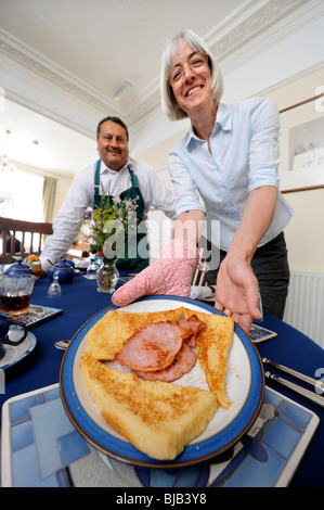 Una coppia che gestisce un bed and breakfast guesthouse servire la prima colazione di toast alla francese e la pancetta per un guest Foto Stock