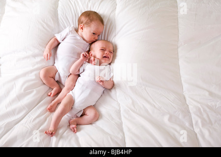 Twin Neonato Neonati affiancati sulla soffice coltre bianca, uno che grida Foto Stock