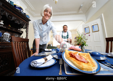 Una coppia che gestisce un bed and breakfast guesthouse servire la prima colazione di toast alla francese e la pancetta per un guest Foto Stock