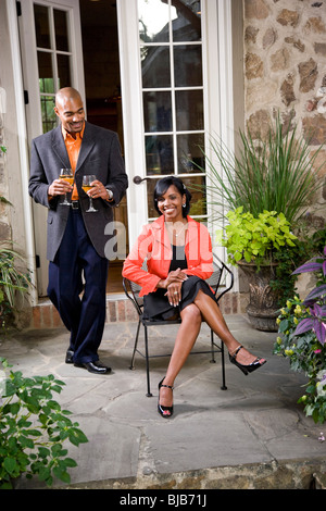 Mid-adulto coppia afro-americano sul patio con giardino, uomo portando fuori del vino Foto Stock