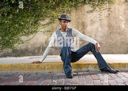 Bello stile afro-americano di giovane uomo seduto sul marciapiede Foto Stock