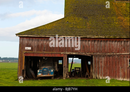 Un vecchio fienile con un vintage carrello parcheggiato sotto il tetto spiovente situato nella valle di Skagit del nord-ovest dello Stato di Washington. Foto Stock