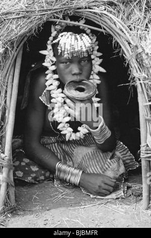 Tribù dei Mursi Ragazza con piastra a labbro Sat nel vano della porta al suo rifugio, Valle dell'Omo, Etiopia Foto Stock