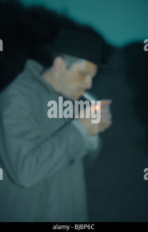 Immagine sfocata di un uomo di accendere una sigaretta , indossando un ranicoat e hat su un vicolo del paese. Foto Stock