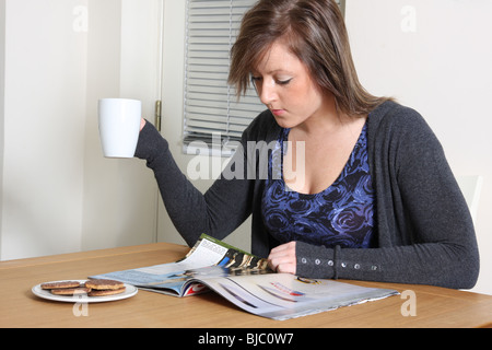 Una giovane donna leggendo una rivista e di bere una bevanda calda. Foto Stock