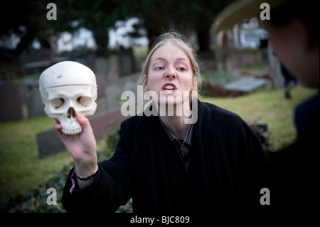 Una donna studente a Aberystwyth University tenendo un cranio di eseguire della scena del cimitero ('ahimè, povero Yorick! Sapevo di lui, Horatio...") in un tutto-femmina lingua gallese traduzione dell'Hamlet di Shakespeare , sulla posizione nella chiesa Llanbadarn cimitero Wales UK Foto Stock