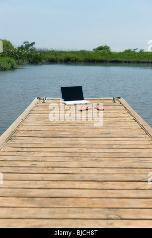 Computer portatile e flip-flop a sinistra sul dock Foto Stock