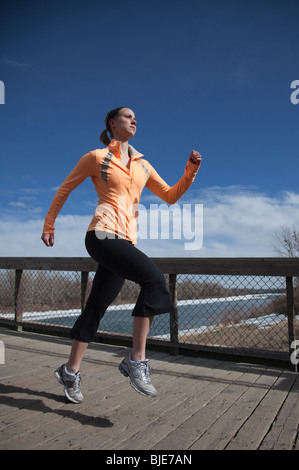 Giovane donna energica che corre all'aperto attraverso il ponte sul fiume in un parco cittadino Foto Stock