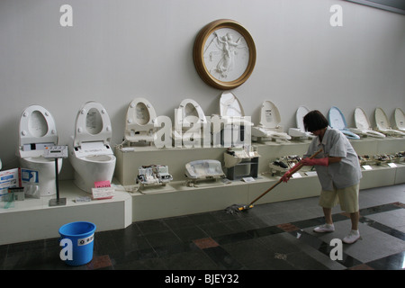 Un dipendente pulisce davanti a un display di vari tipi di bagni, nei laboratori di ricerca della Toto. Kokura, Giappone. 2005. Foto Stock