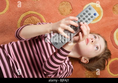 Giovane ragazza cambiare canale con il telecomando della TV Foto Stock