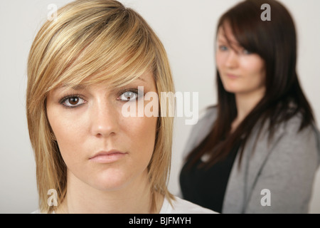 Due ragazze in piedi in un studio la ragazza dietro al di fuori della messa a fuoco guardando il retro della ragazza di fronte. Foto Stock