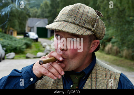 Uomo in tweed e Deerstalker Hat di fumare un sigaro nelle Highlands della Scozia Foto Stock