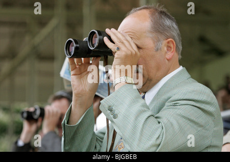 Un uomo che guarda attraverso il binocolo a corse di cavalli, Iffezheim, Baden-Württemberg Foto Stock