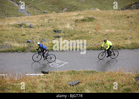 Immagine a colori. Guardando verso il basso a partire da sopra, due ciclisti su strada su un paese formazione ciclo di marcia fino a umido su strada di montagna. Foto Stock
