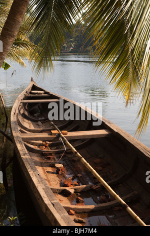 India Kerala, Alleppey, Alappuzha, backwaters piccola barca di legno ormeggiata su riverbank sotto coconut Palm tree Foto Stock