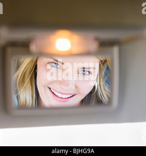 Donna che guarda nella visiera specchio in auto Foto Stock
