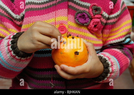 Giovane ragazza che indossa un colorato luminosamente cardigan rendendo un pomander, spingendo i chiodi di garofano in un arancione a Natale, il Galles. Foto Stock