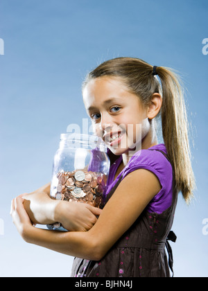 Ragazza guardando la telecamera tenendo un barattolo di monete Foto Stock