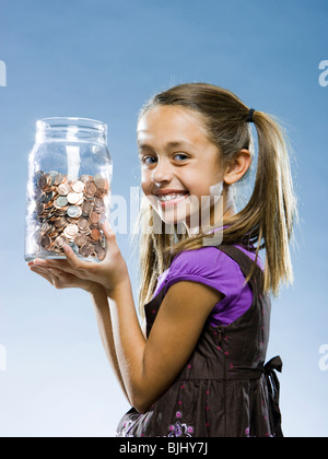 Ragazza guardando la telecamera tenendo un barattolo di monete Foto Stock