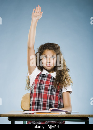 Schoolgirl alla scrivania con braccio sollevato Foto Stock