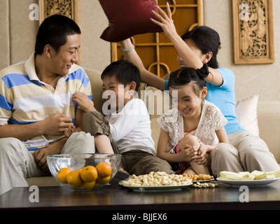 Famiglia avente pillow fight sul divano a ridere Foto Stock