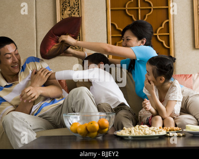 Famiglia avente pillow fight sul divano a ridere Foto Stock