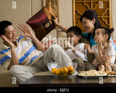 Famiglia avente pillow fight sul divano a ridere Foto Stock