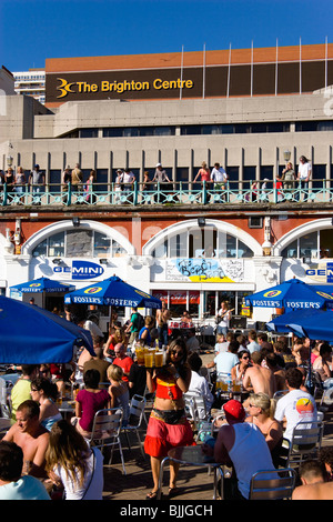 Inghilterra, East Sussex, Brighton gente seduta sotto la pantina parasole ombrelli a tabelle sul lungomare al di fuori della Gemini Bar in spiaggia Foto Stock