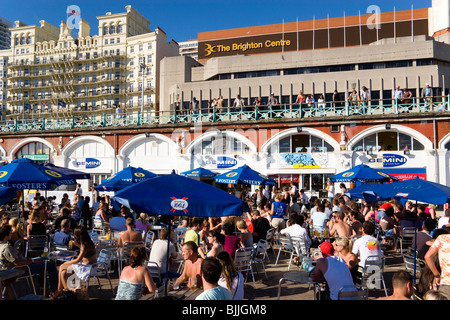 Inghilterra, East Sussex, Brighton gente seduta sotto la pantina parasole ombrelli a tabelle sul lungomare al di fuori della Gemini Bar in spiaggia Foto Stock