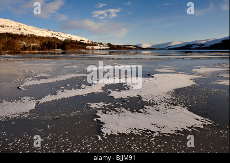 Congelati Loch Tay con circostante coperta di neve sulle colline vicino a Killin, Perthshire, Scotland, Regno Unito Foto Stock
