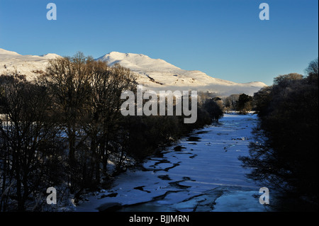 La congelati e alberato River Dochart con snowclad lontane montagne vicino a Killin, Perthshire, Scotland, Regno Unito Foto Stock