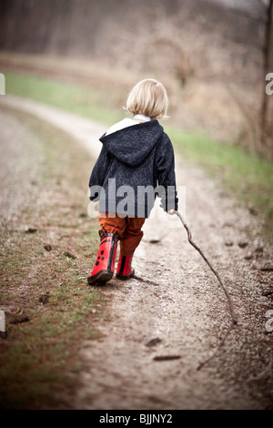 Giovane ragazzo indossare stivali da pioggia passeggiate attraverso una pozza d'acqua. Foto Stock