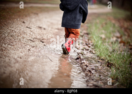 Giovane ragazzo indossare stivali da pioggia passeggiate attraverso una pozza d'acqua. Foto Stock