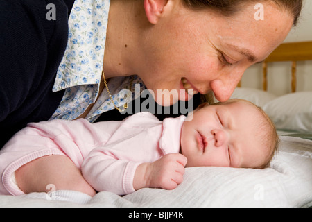 Mamma sorride / sorridente al suo sonno / addormentato new born baby, sul letto / culla. Foto Stock