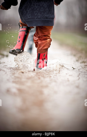 Giovane ragazzo indossare stivali da pioggia passeggiate attraverso una pozza d'acqua. Foto Stock