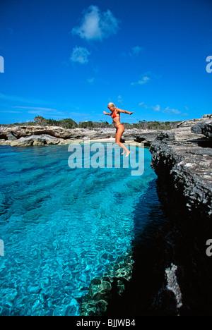 Isole Turks e Caicos, Providenciales, donna salta fuori da parete di roccia in bikini rosso a punto nordovest Foto Stock