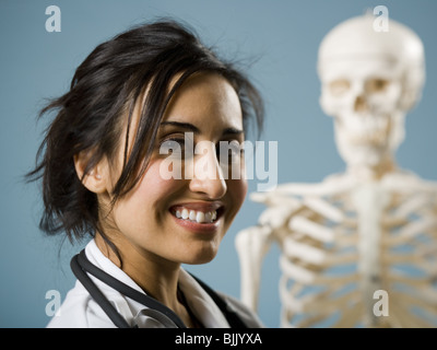 Medico donna sorridente con scheletro in background Foto Stock