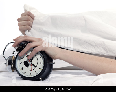 Giovane donna donna nel letto risveglio stanco tenendo sveglia su sfondo bianco Foto Stock