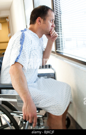 Uomo in abito ospedale seduto nella sedia guardando attraverso la finestra Foto Stock