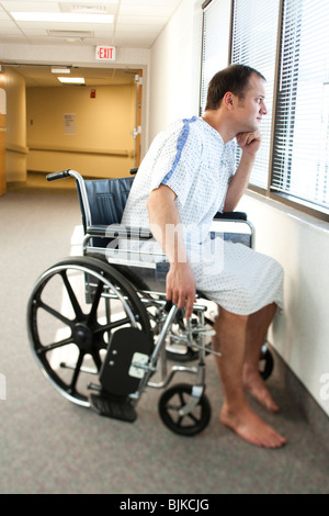 Uomo in abito ospedale seduto nella sedia guardando attraverso la finestra Foto Stock