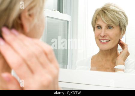 La riflessione di donna matura nello specchio del bagno Foto Stock
