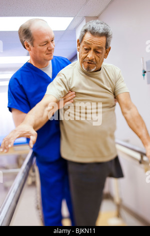 Fisioterapista assistere un uomo anziano con una gamba in piedi Foto Stock