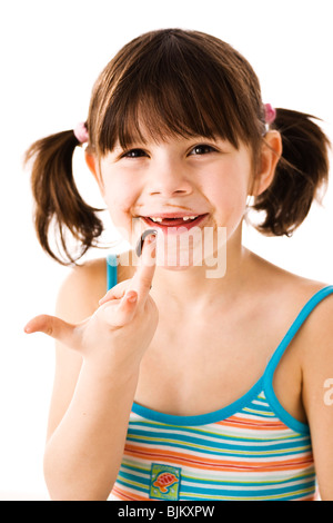 Bambina con pig-tail leccare il cioccolato il suo dito Foto Stock