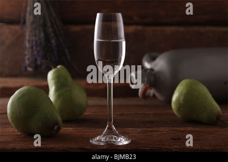 Bicchiere di acquavite di pere con pere e un vaso di whiskey su un rustico sfondo di legno Foto Stock