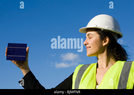 Donna in hard hat tenendo una cella solare di fronte a un cielo blu Foto Stock